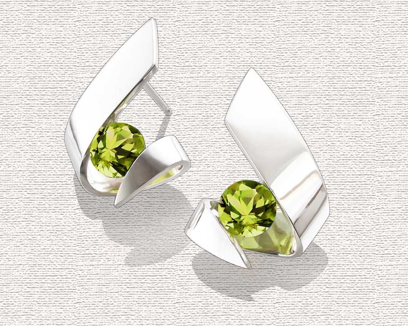 Puede incluir: Un par de pendientes de plata con una piedra preciosa verde en cada uno. Los pendientes tienen forma de cinta retorcida.