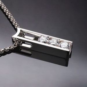 May include: A silver necklace with a pendant featuring three round diamonds set in a vertical bar design.