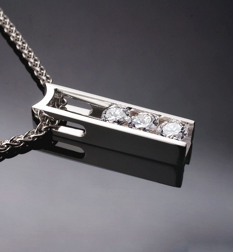 May include: A silver necklace with a pendant featuring three round diamonds set in a vertical bar design.