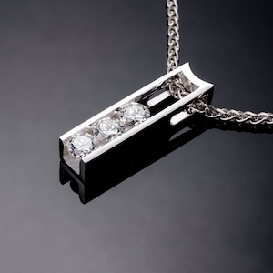 May include: A silver pendant necklace with a rectangular bar design featuring three clear round gemstones. The chain is a silver rope chain.