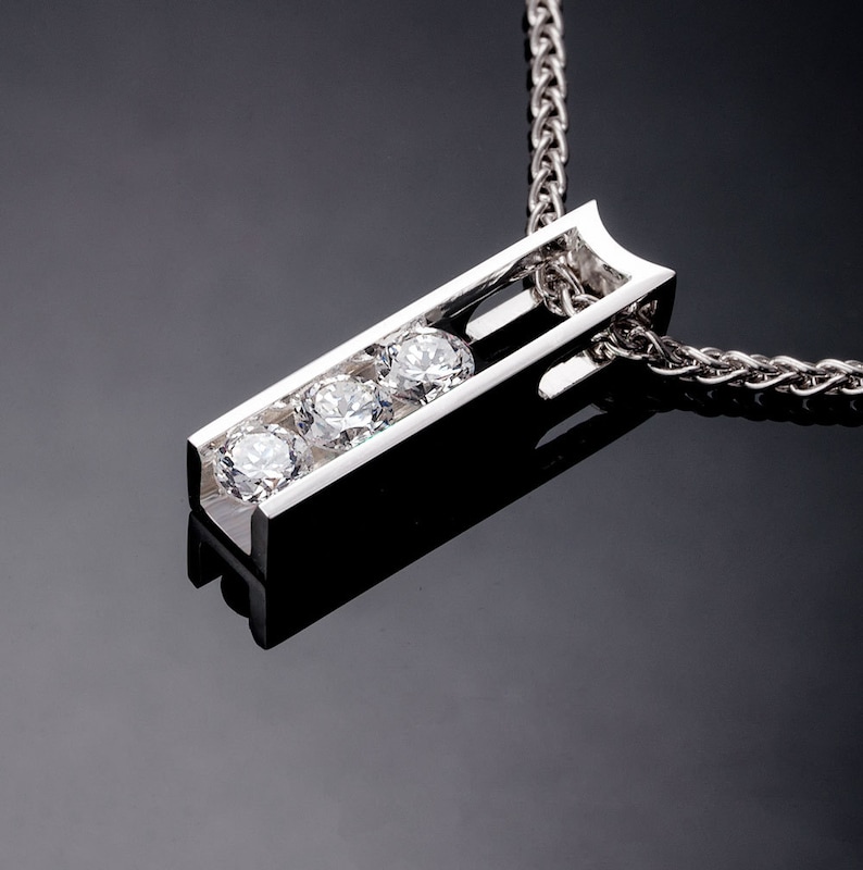 May include: A silver pendant necklace with a rectangular bar design featuring three clear round gemstones. The chain is a silver rope chain.