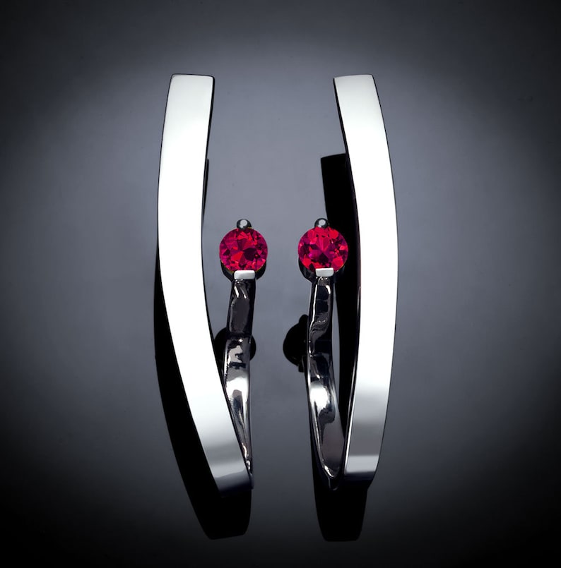 May include: A pair of silver earrings with a single red gemstone on each earring.