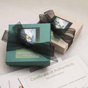 May include: Two teal and beige gift boxes with black ribbon bows. The boxes have a white label with the text "VerbenaPlace etsy.com". A certificate of authenticity is visible in the background.