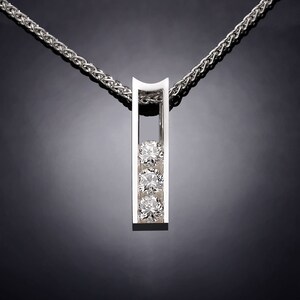 May include: A silver pendant necklace with a vertical bar design featuring three round diamonds. The diamonds are set in a row within the bar.