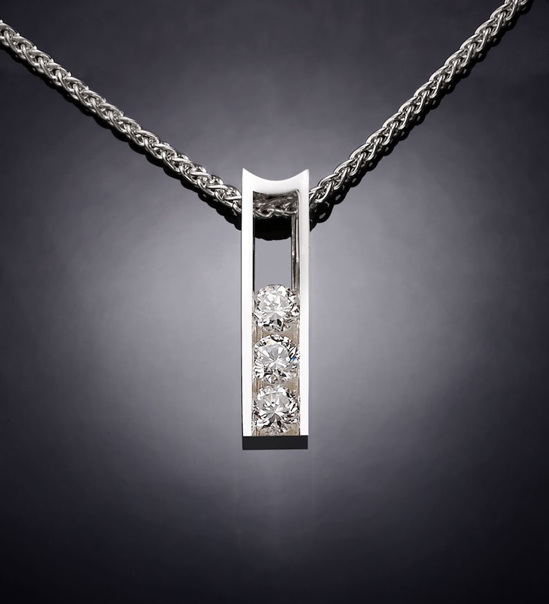May include: A silver pendant necklace with a vertical bar design featuring three round diamonds. The diamonds are set in a row within the bar.
