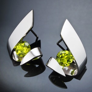 Puede incluir: Un par de pendientes de plata con una piedra preciosa verde en cada uno. Los pendientes tienen forma de dise&ntilde;o abstracto curvado.