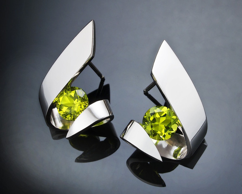 Puede incluir: Un par de pendientes de plata con una piedra preciosa verde en cada uno. Los pendientes tienen forma de dise&ntilde;o abstracto curvado.