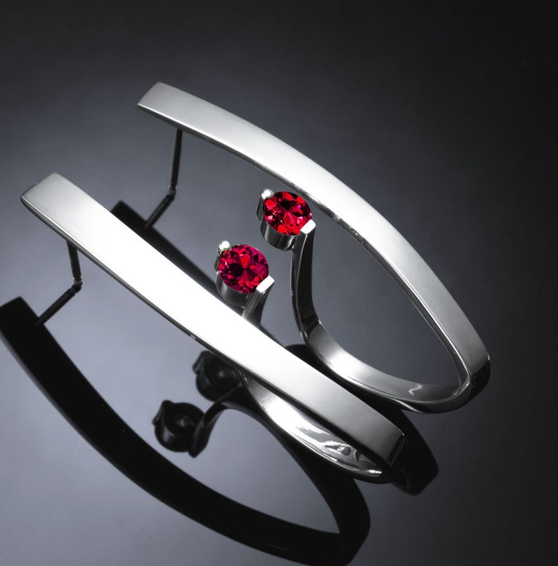 May include: A pair of silver earrings with a curved design and two red gemstones.