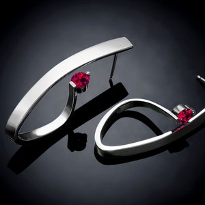 May include: A pair of silver earrings with a curved design and a single red gemstone on each earring.