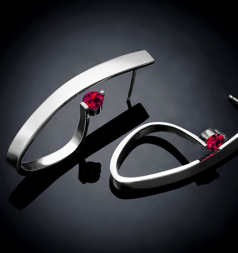 May include: A pair of silver earrings with a curved design and a single red gemstone on each earring.