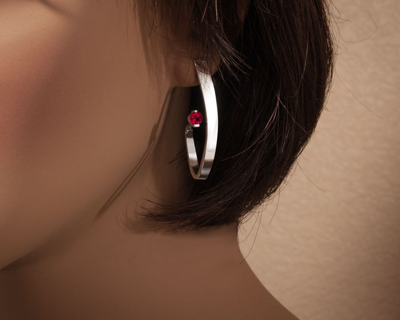 May include: Silver hoop earrings with a single red gemstone accent.