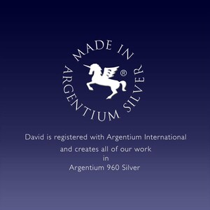 May include: A white logo with a unicorn and the text "MADE IN ARGENTIUM SILVER" in a circle. The text "David is registered with Argentium International and creates all of our work in Argentium 960 Silver" is below the logo.