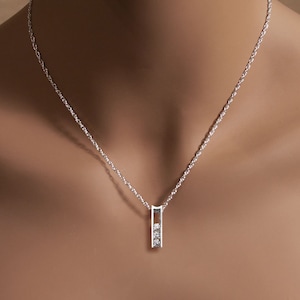 May include: A silver chain necklace with a small pendant featuring three clear diamonds set in a vertical bar.
