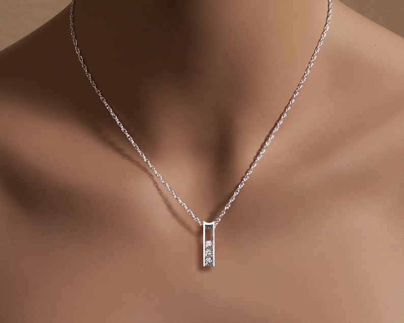 May include: A silver chain necklace with a small pendant featuring three clear diamonds set in a vertical bar.