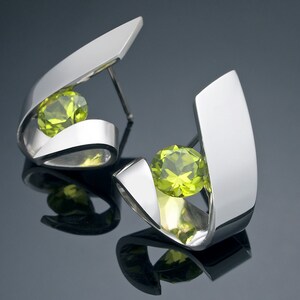 Puede incluir: Un par de pendientes de plata con una piedra preciosa verde en cada uno. Los pendientes est&aacute;n hechos de dos piezas curvas de metal que se cruzan para crear un dise&ntilde;o &uacute;nico.