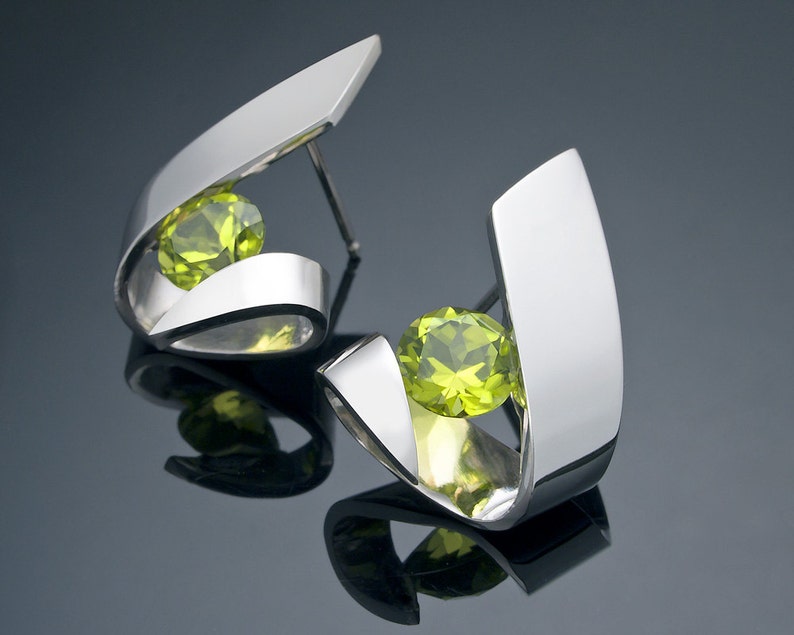 Puede incluir: Un par de pendientes de plata con una piedra preciosa verde en cada uno. Los pendientes est&aacute;n hechos de dos piezas curvas de metal que se cruzan para crear un dise&ntilde;o &uacute;nico.