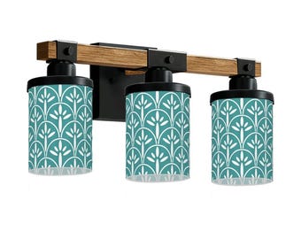 May include: A three-light vanity fixture with a wood-tone beam and black metal accents. The cylindrical shades feature a teal and white floral pattern. The fixture is designed for wall mounting.