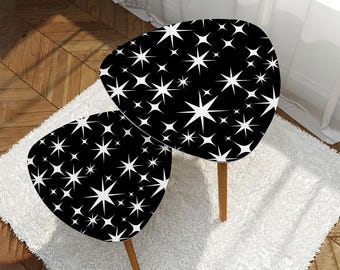 May include: Two black and white starburst patterned side tables. The tables have a rounded triangular shape with wooden legs. They are placed on a white fluffy rug.