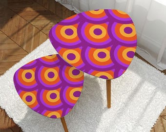 May include: Two retro-style side tables with a purple, orange, and yellow circular pattern on the tabletop. The tables have a unique, rounded triangular shape and are supported by wooden legs. The tables sit on a white rug.