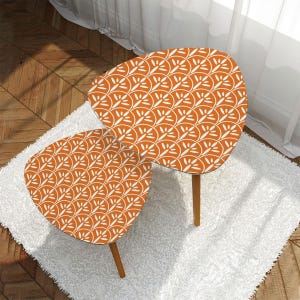 May include: Two matching orange and white patterned side tables with wooden legs. The tables have a unique, rounded triangular shape and are placed on a white shag rug. The tables are a decorative accent for a living room or bedroom.