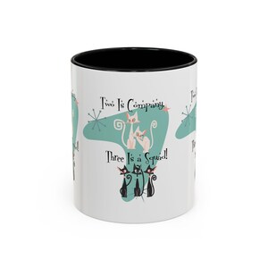 May include: White ceramic mug with a black interior. The mug features a retro design with the text "Two Is Company, Three Is a Squad!" and illustrations of cats in a mid-century modern style.