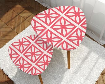 May include: Two nesting side tables with a white and coral geometric floral pattern on the tabletop. The tables have a teardrop shape and are supported by three wooden legs. The tables are placed on a white rug.