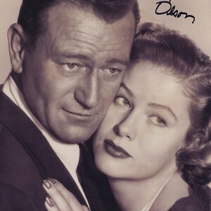 Peut inclure: Une photographie vintage en noir et blanc montrant un homme en costume et une femme aux cheveux ondulés appuyée contre lui. L'image comporte la signature manuscrite Nancy Olson dans le coin supérieur droit, écrite à l'encre noire sur le fond clair.