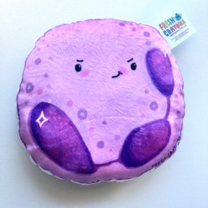 May include: A plush purple pillow shaped like a cell with a cartoon face and two purple bean-shaped organelles. The pillow has a white background with small purple dots and the text "FRESH CRAYONS" on the bottom right corner.