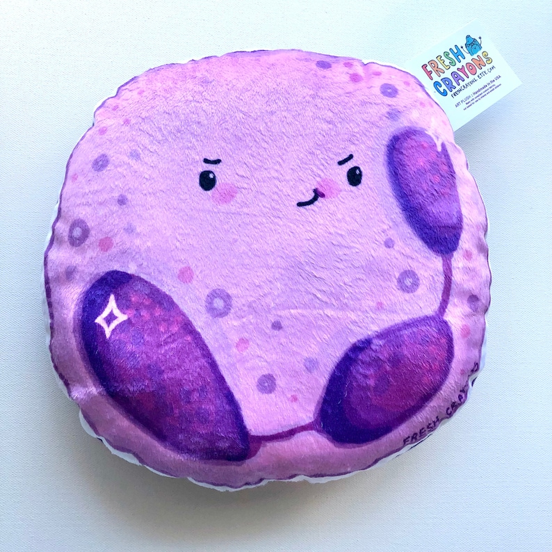 May include: A plush purple pillow shaped like a cell with a cartoon face and two purple bean-shaped organelles. The pillow has a white background with small purple dots and the text "FRESH CRAYONS" on the bottom right corner.