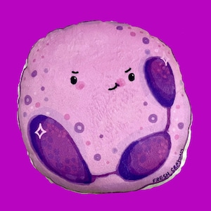 May include: A plush toy shaped like a purple and pink cell with a winking face and the text "FRESH CRAYONS" on the bottom.