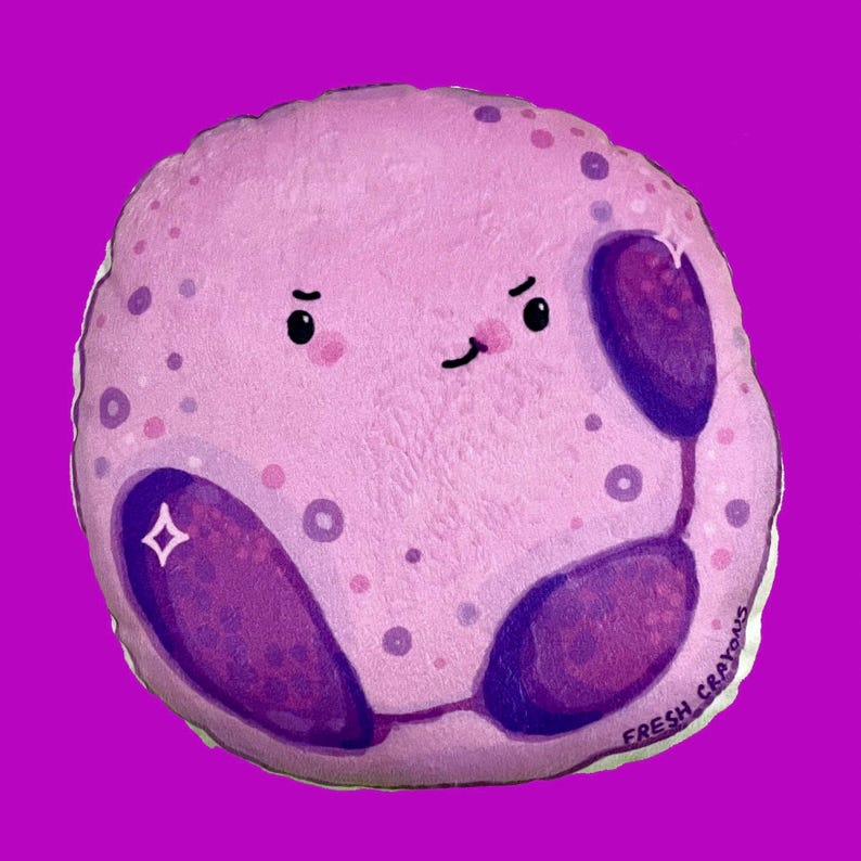 May include: A plush toy shaped like a purple and pink cell with a winking face and the text "FRESH CRAYONS" on the bottom.