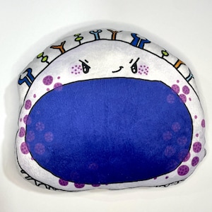 May include: White plush toy shaped like a cell with a blue nucleus and purple dots. The cell has a cartoon face with angry eyebrows and a smile.