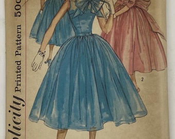 May include: Vintage Simplicity printed pattern featuring illustrations of three dresses. The dresses are in blue and pink, with a bow detail on the bodice. The pattern is marked with the number 1877 and the price 50c.