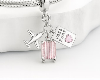 May include: A silver charm bracelet with a travel-themed charm. The charm features a small airplane, a pink suitcase, and a passport tag with a heart. The suitcase is pink with vertical stripes. The passport tag has the word "PASS PORT".