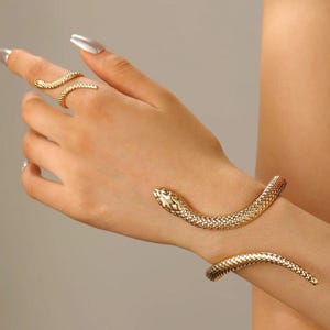 May include: Gold-toned snake-shaped jewelry set. The set includes a ring and a bracelet. The ring wraps around a finger, and the bracelet wraps around the wrist. The jewelry has a textured, scale-like pattern.