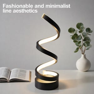 May include: A black and gold spiral LED desk lamp with the text "Fashionable and minimalist line aesthetics". The lamp has a modern design and is next to an open book and a vase with greenery.