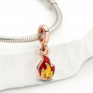 May include: A rose gold charm in the shape of a flame, with red and yellow enamel detailing. The charm is attached to a silver bracelet. The flame charm is a jewelry accessory.