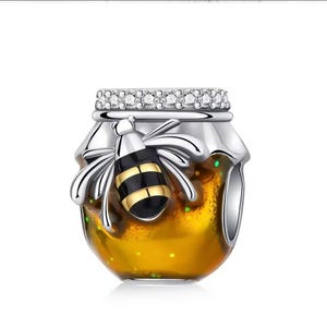 Peut inclure: Un charm en argent représentant un pot de miel et une abeille. Le pot contient un liquide jaune et possède un couvercle orné de pierres transparentes. L'abeille est noire et dorée. Le charm est pour un bracelet ou collier.