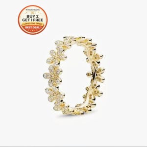 May include: A gold-colored ring featuring a floral design. The ring is adorned with small, clear gemstones set within each flower. The ring's design is a continuous pattern of flowers around the band. The background is a solid white.