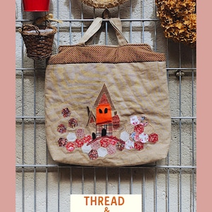 Peut inclure: Un sac fourre-tout beige avec un motif patchwork représentant une maison orange et des accents floraux rouges, blancs et roses. Le sac a une bordure et des poignées à pois marron. Le texte "THREAD & MEMORY" est affiché en bas.