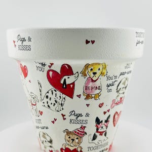 May include: White ceramic flower pot decorated with cartoon dogs, hearts, and the phrases "Pugs & Kisses," "Be Mine," and "Together fur-ever." The pot features a variety of dog breeds and Valentine's Day themed illustrations.