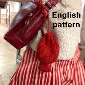 Könnte beinhalten: Eine rote Ledertasche mit Reißverschluss und einem kleinen roten Strickbeutel, der daran hängt. Der Text "English pattern" ist sichtbar. Die Person trägt eine rot-weiß gestreifte Hose.