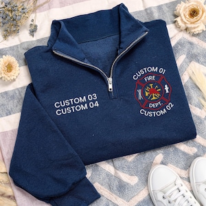 May include: A navy blue quarter-zip sweatshirt featuring white embroidered text that reads CUSTOM 03 CUSTOM 04 on the left chest and a red and white embroidered fire department emblem on the right chest with the text CUSTOM 01 FIRE DEPT. CUSTOM 02.