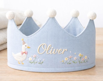 May include: A light blue fabric crown-shaped storage basket with white pom-poms and embroidered details. Features a cartoon duck wearing a party hat and the name "Oliver" in cursive, with floral accents.