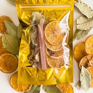 May include: A gold resealable bag filled with dried orange slices, cinnamon sticks, and bay leaves. The bag is surrounded by more dried orange slices and bay leaves.