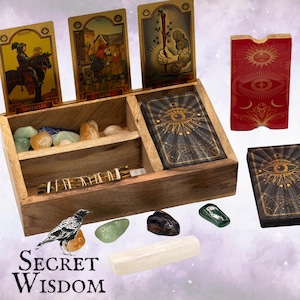 Puede incluir: Un juego de caja de madera con cartas del tarot, cristales y una vara de incienso. El juego incluye cartas ilustradas, una baraja con un diseño de ojo y una caja de madera para guardar. Las palabras "Secret Wisdom" están impresas en la parte inferior.