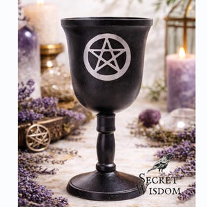 May include: Black chalice featuring a silver pentagram. The goblet has a wide rim, a slender stem, and a round base. The chalice is part of a collection of spiritual and Wiccan items.