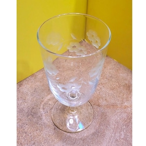 May include: Clear glass goblet with etched floral design. The glass has a slender stem and a wide, rounded bowl. The floral pattern is repeated around the bowl. Suitable for serving water, wine, or other beverages.
