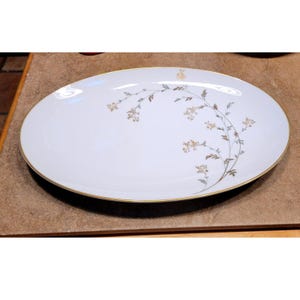 May include: Oval white serving platter with a gold rim and a delicate floral design in gold and brown. The platter has a smooth surface and is suitable for serving various dishes.