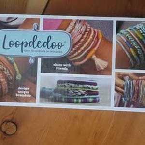 Può includere: Una scatola con la scritta "Loopdedoo" in una cornice azzurra. La scatola mostra immagini di braccialetti colorati, con il testo "design unique bracelets" e "share with friends". I braccialetti sono fatti di fili colorati.